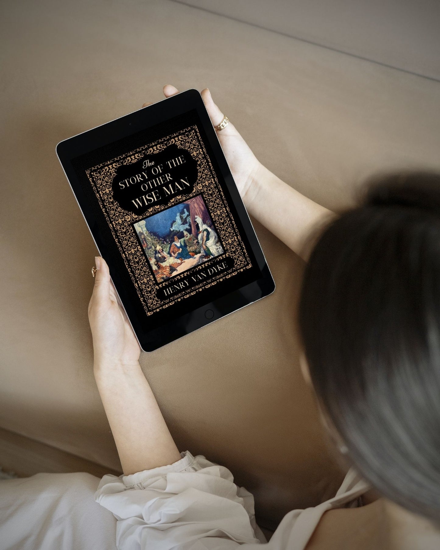 A dark haired woman holds a black tablet with the ornate black and gold cover of the ebook "The Story of the Other Wise Man."