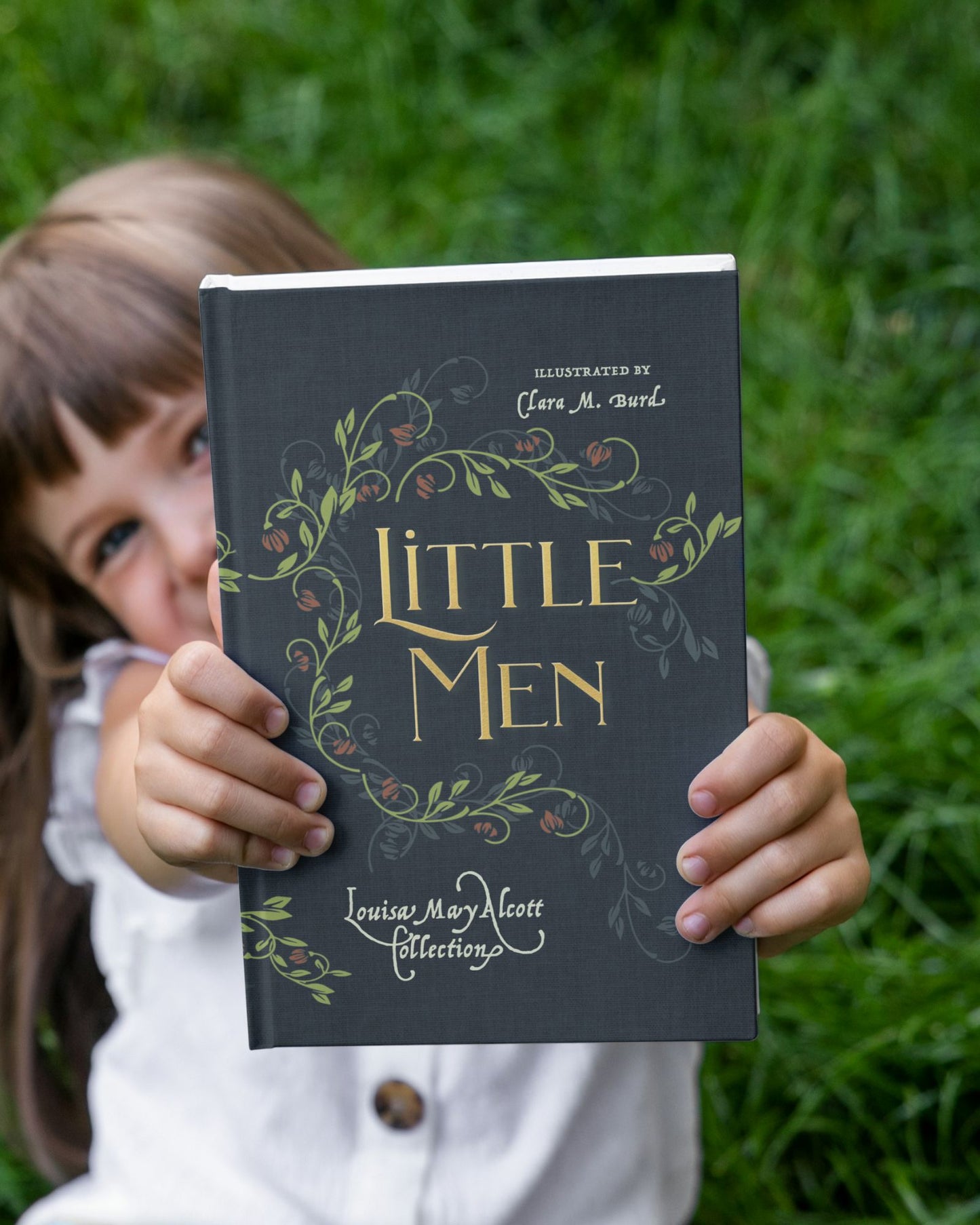 A happy young girl holding a beautiful hardcover edition of Little Men by Louisa May Alcott, published by Smidgen Press. Illustrations by Clara M. Burd.