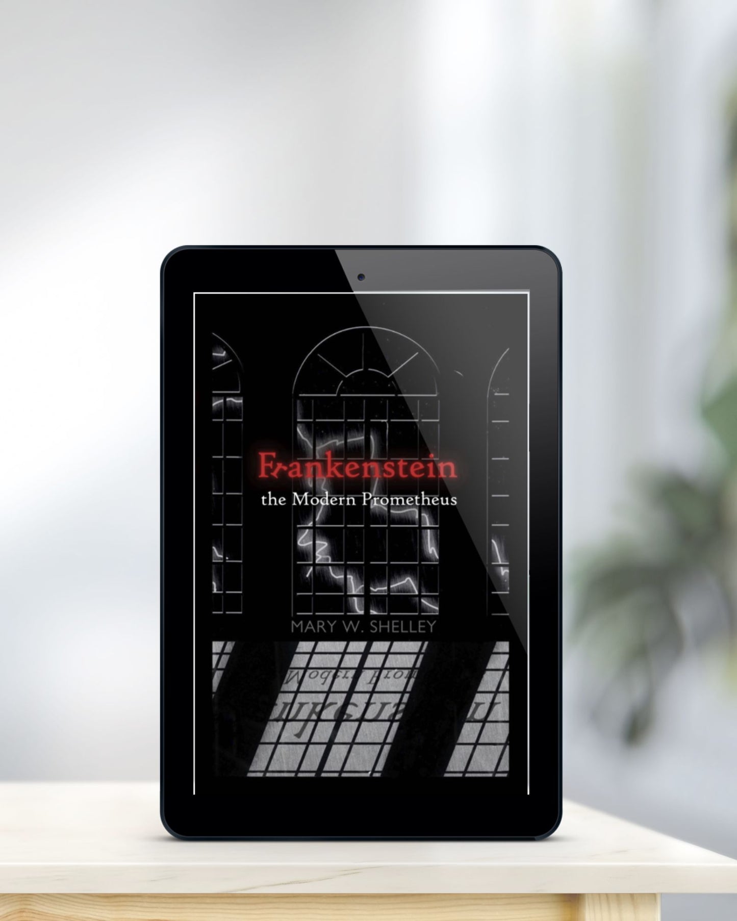 Tablet displaying black ebook cover of "Frankenstein: the Modern Prometheus" is standing on a blonde table in front of blurred background.