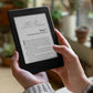 White hands gently hold a tablet which is turned to the illustrated heading for chapter 7 in the ebook of "The Prisoner of Zenda". The background of this picture is blurred plants on the floor and on a windowsill. 
