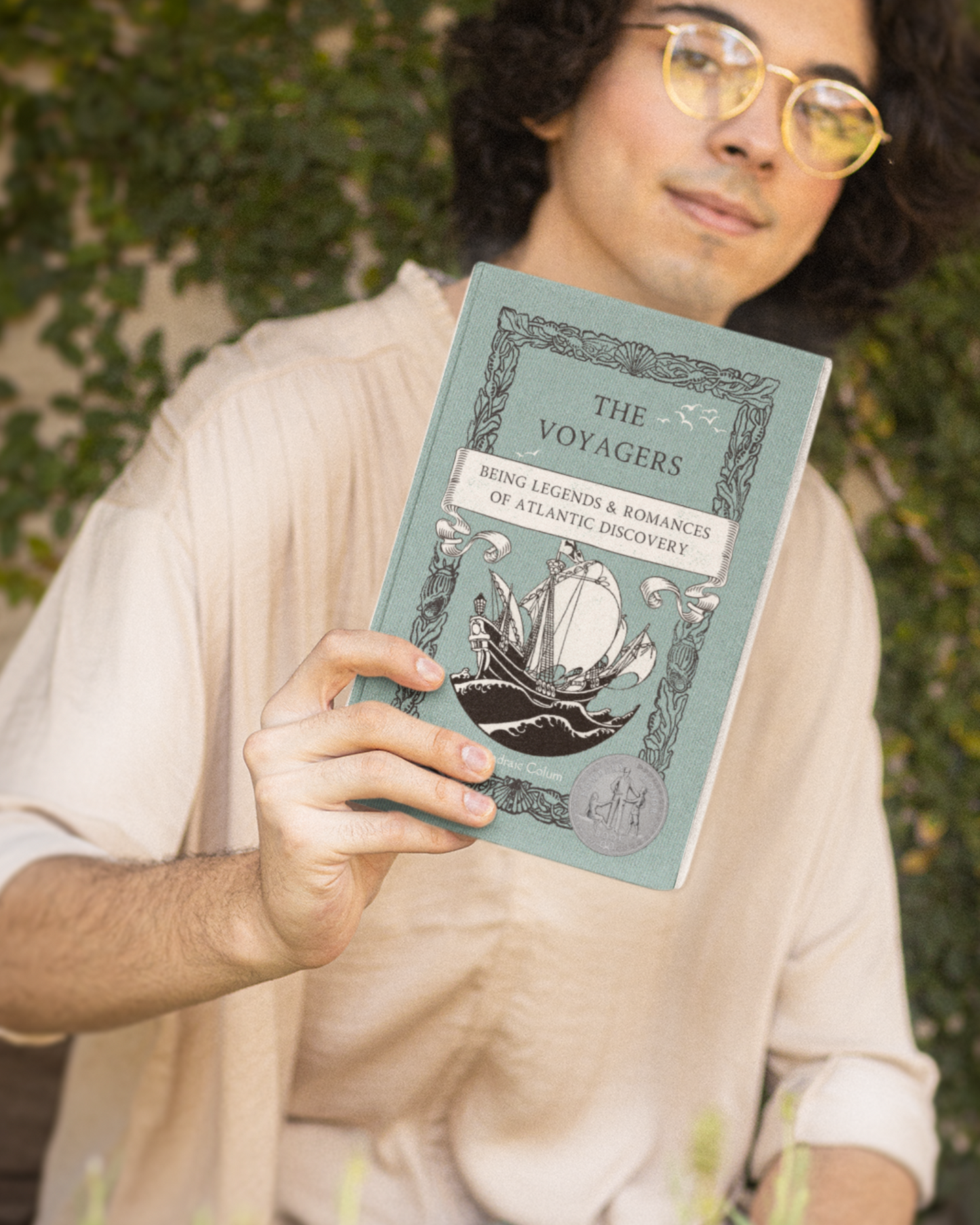 Paperback with teal cover of "The Voyagers: Being Legends & Romances of Atlantic Discovery" held by dark-haired young man in front of a wall of vines.