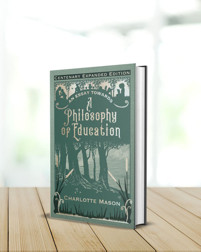 A hardback of the sage green book "An Essay towards a Philosophy of Education" stands on a blonde table with the background blurred.