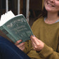 A smiling white girl in jeans and a gold sweater smiles while holding open the paperback edition of the sage colored An Essay Towards A Philosophy of Eduction.