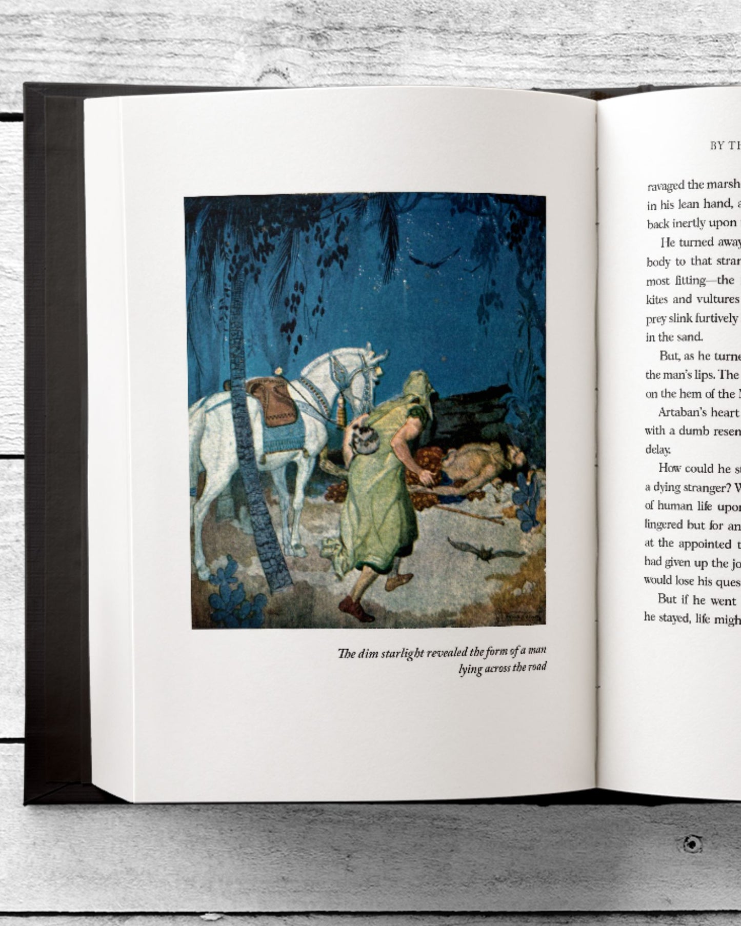 An inside peek into one of the restored illustrations within the ornate book "The Story of the Other Wise Man" and in the picture a white horse and his owner carefully approach a wounded man. The book lies open to this page resting on a rustic white table.