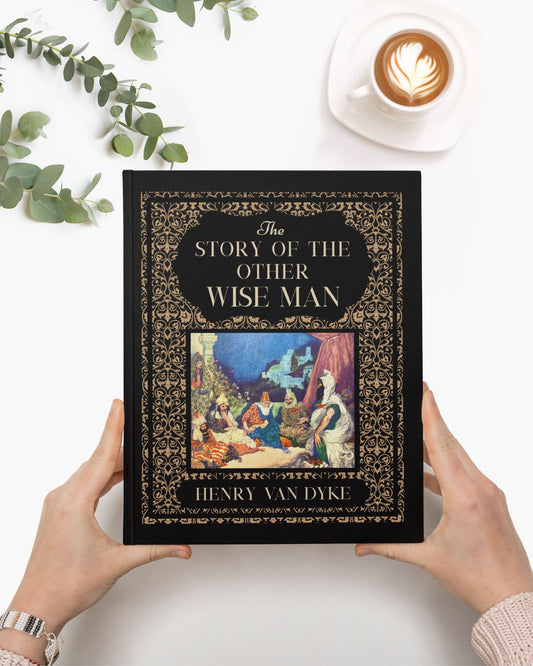 The ornate and illustrated copy of The Story of the Other Wise man is being held by a woman's white hands in front of a blank white surface. Nearby is a mug of coffee with swirled cream and branches of eucalyptus.